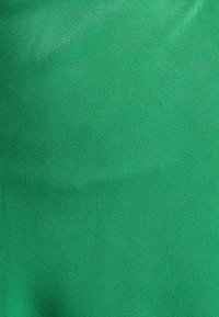 Textured green fabric featuring a smooth finish, characterized by a solid color with a slightly reflective surface. No patterns or accents.