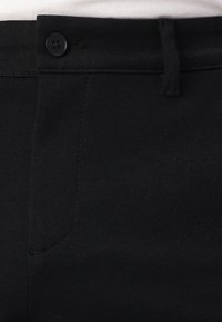 I pantaloni neri presentano una superficie in tessuto liscia, una chiusura con bottone standard e una discreta cucitura lungo il lato.
