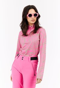 Camiseta de manga larga en rosa claro con patrón abstracto de cebra en rosa más oscuro; cuello alto. Pantalones ajustados rosas con acentos negros y bolsillos con cremallera.