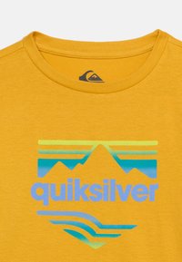 Κίτρινο T-shirt με λογότυπο βουνών σε μπλε και πράσινο και το κείμενο «quiksilver» στο στήθος κάτω από στρογγυλή λαιμόκοψη.