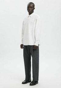 Langermet skjorte med hvite striper og krage, kombinert med mørkegrå bukser og svarte sko, vist mot en nøytral bakgrunn.