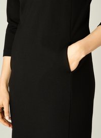 Zwarte jurk met driekwartmouwen, een zijzak en een elegante, gladde textuur. Het ontwerp is figuurvormend en minimalistisch.