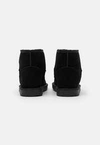 Botines de ante negro con una textura suave, punta redondeada y suela de goma baja. Presentan un sencillo detalle de costura y un borde liso.