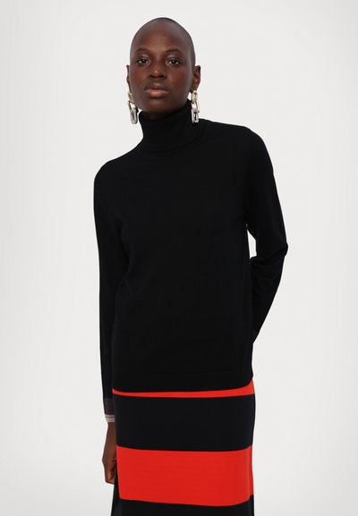 Pull à col roulé noir à manches longues, associé à une jupe à rayures verticales aux couleurs rouge, noir et blanc. Texture lisse.