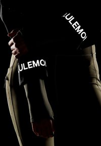 Sort langærmet top med teksturerede, ribbede manchetter, der har hvid "LULULEMON" branding, parret med tætsiddende olivengrønne bukser med lynlås.