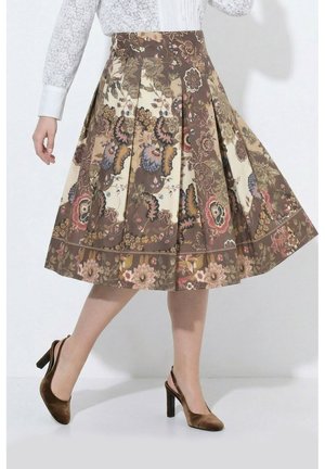 Frau trägt einen plissierten Midirock mit braunen Blumenmustern und braune Velours-Slingback-Pumps mit hohen Absätzen, steht vor weißem Hintergrund.