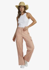 Lyserøde cargo bukser med sidelommer, parret med en hvid ribbet tanktop og en stråhat. Modellen bærer hvide sneakers.