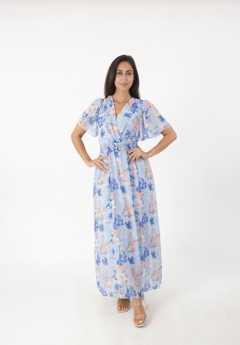 Robe maxi en tissu bleu clair avec des motifs floraux roses et bleus. Manches courtes et bouffantes avec une taille cintrée. Talons transparents.