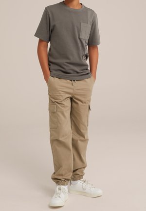 Camiseta de punto gris de manga corta con bolsillo en el pecho, combinada con pantalones cargo beige con puños elásticos y bolsillos laterales, completada con zapatillas blancas.