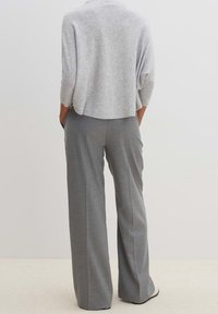 Šedý pletený svetr v kombinaci s světle šedými kalhotami s širokými nohavicemi. Svetr má uvolněný střih a 3/4 rukávy; kalhoty mají hladkou texturu.