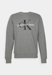 Gray sweatshirt made of soft material, featuring a crew neck, ribbed cuffs, and a graphic logo reading “Calvin Klein Jeans” in black and white.