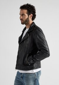 Schwarze Leder-Bikerjacke mit slim fit, asymmetrischem Reißverschluss und seitlichen Taschen. Verfügt über eine glatte Textur und ein breites Kragen-Design.