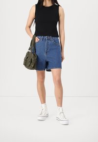 Black sleeveless top, high-waisted blue denim shorts, olive green shoulder bag, and white high-top sneakers with black accents.