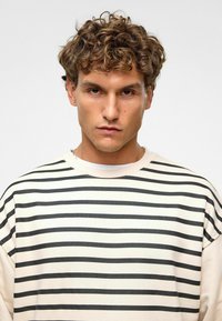 Gestreept sweatshirt met horizontale zwarte strepen op een roomkleurige achtergrond, met een ontspannen pasvorm en ronde hals. 