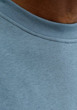 Blå bomullstyg med en slät textur, försedd med en ribbad halskant. Närbilden visar fina vävdetaljer.