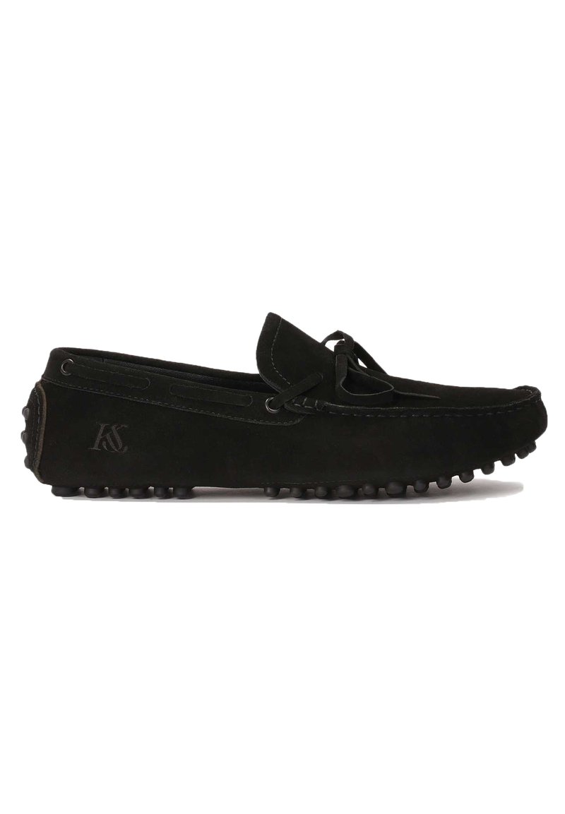Mocasines de ante negro con punta redondeada, detalle de cordones y suela de goma texturizada. Presenta un logo grabado en el talón para una marca sutil.