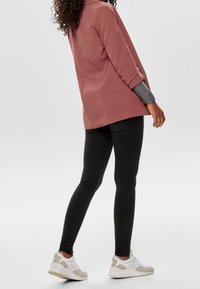 Long-sleeve pink blazer with a subtle texture, paired with black skinny jeans and gray-and-white sneakers. Simple cut and relaxed fit.