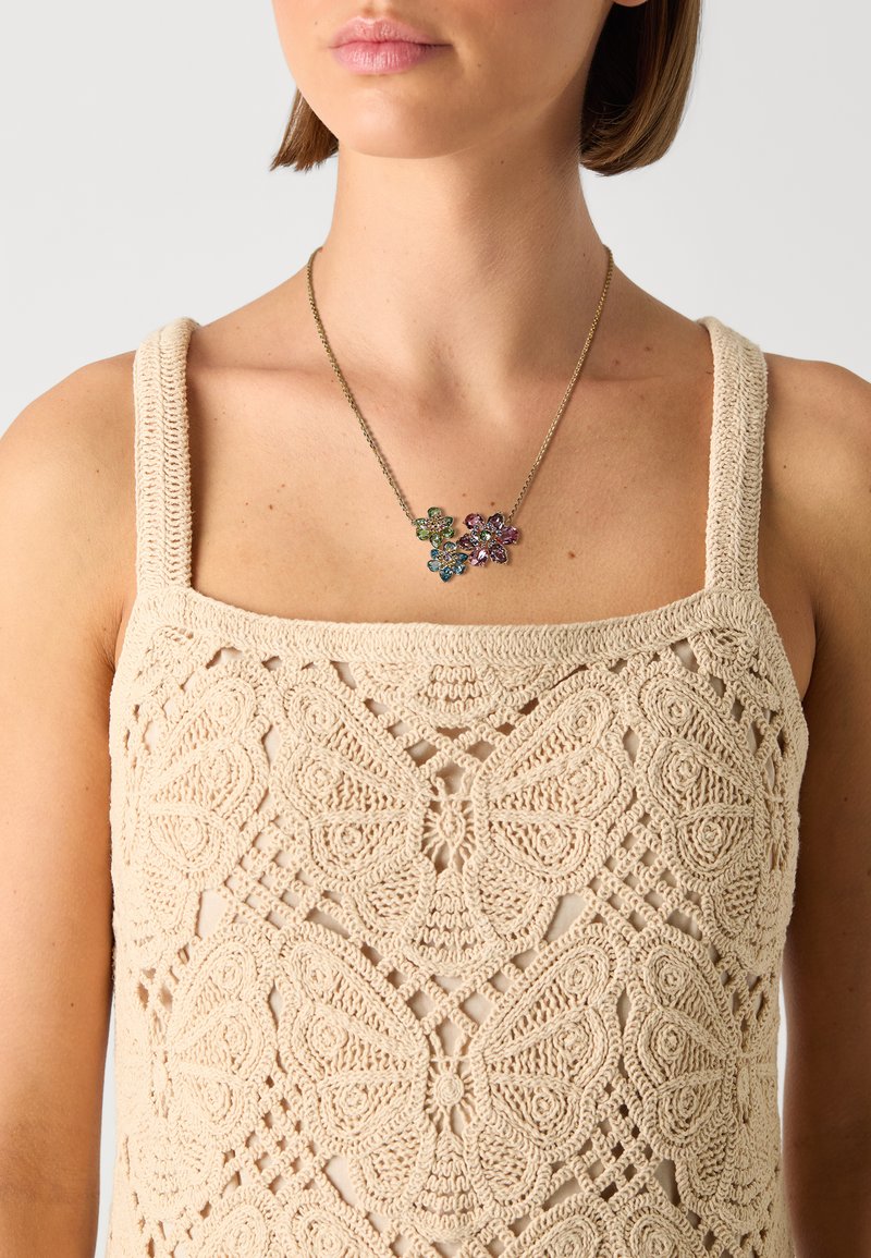 Beige hæklede tanktop med blomstret blondermønster. Guld halskæde med farverige ædelstene i blomsterformer.