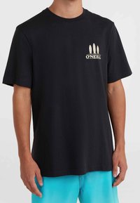 Mand iført en sort O'Neill t-shirt med tre surfbræt ikoner og logo på venstre bryst, parret med lyseblå shorts.