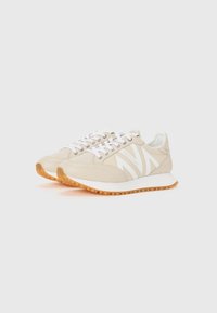 Baskets d'athlétisme beiges avec des accents blancs, présentant une semelle texturée et des lacets, conçues avec une silhouette rétro de course.