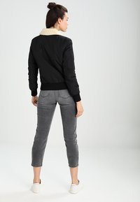Giubbotto bomber nero con colletto in pelliccia sintetica crema, polsini e vita a coste, abbinato a jeans grigi a vita alta e sneakers bianche.