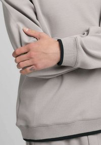 Felpa grigio chiaro con design rilassato; presenta dettagli neri su polsini e orlo. Tessuto liscio, vestibilità leggermente ampia sulle braccia.