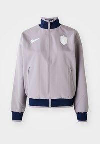 Nike jacket in light gray fabric with a stand-up collar. Features navy blue ribbed cuffs and hem, side pockets, and a white logo emblem.