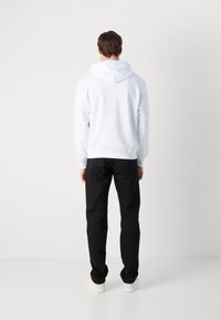 Felpa bianca con cappuccio, dotata di orlo e polsini a costine, abbinata a pantaloni neri e sneakers bianche; design semplice senza motivi o accenti.