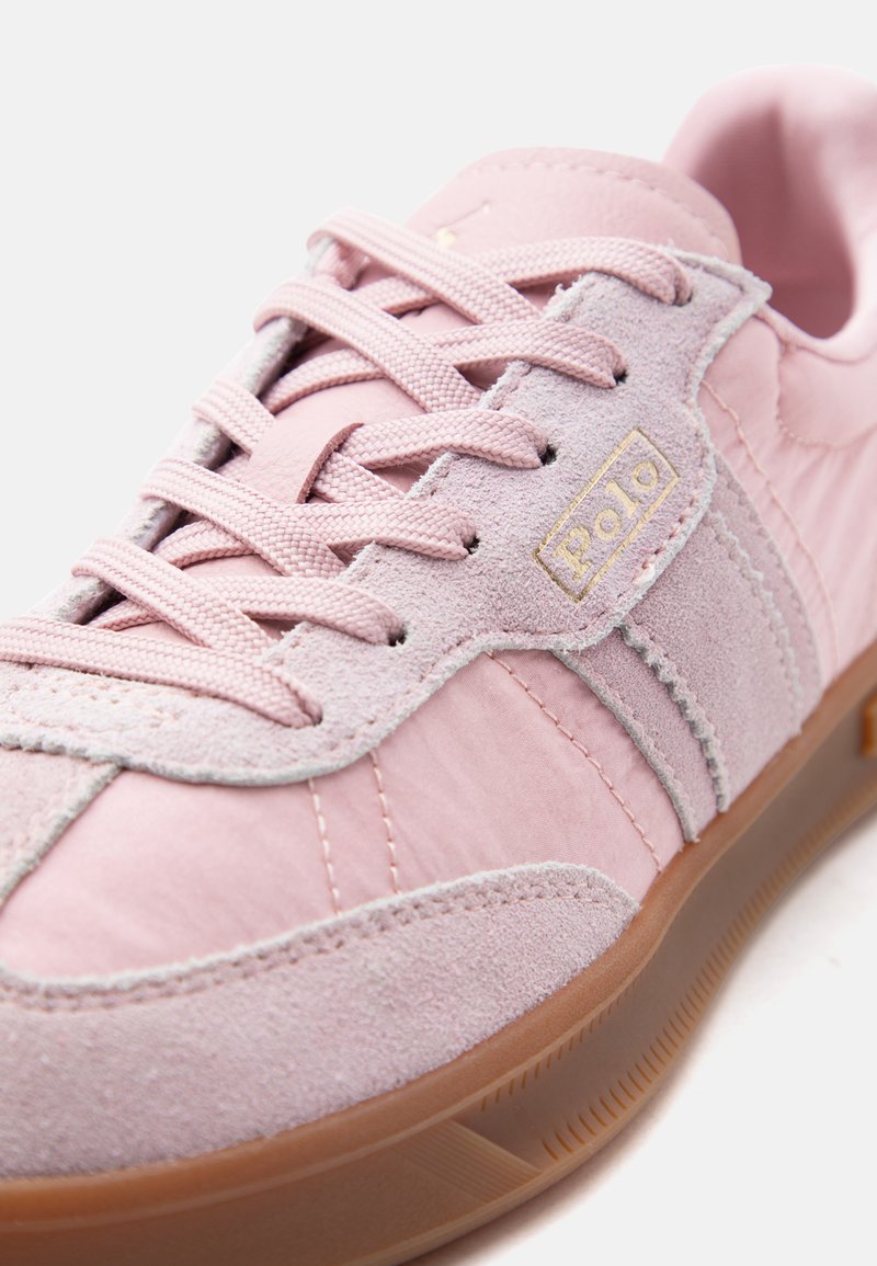 Baskets en daim et tissu rose avec des lacets rose pâle, logo "Polo" beige sur le côté, et semelle en caoutchouc marron clair.
