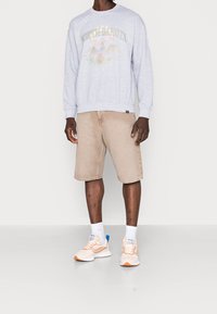 Sudadera gris con gráficos de "NORTH DAKOTA", pantalones cortos beige y zapatillas ligeras con acentos naranjas. Incluye calcetas blancas. Atuendo casual.