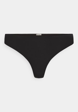 Tanga fără cusături Calvin Klein neagră, cu etichetă pe talie, prezentată întinsă pe un fundal alb.
