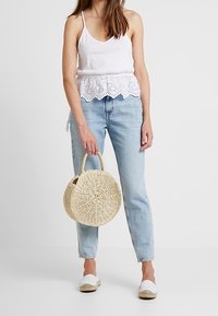 Vit bomullstopp med spetsdetaljer, ljusblå högmidjade jeans, rund halmhandväska och vita espadrilles.