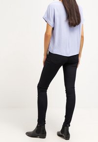 Blusa azzurro chiaro a maniche corte abbinata a jeans neri aderenti e stivali alla caviglia neri. Tessuto liscio, vestibilità rilassata e linee pulite.