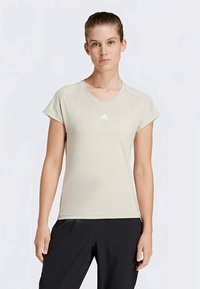 Gai bēšā V-veida T-kreklā ar īsām piedurknēm, izgatavots no mīksta auduma. Uz krūtīm ir neliels balts Adidas logo. Vienkāršs dizains.