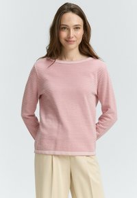 Top rosa chiaro a maniche lunghe con strisce orizzontali, scollatura rotonda e tessuto testurizzato. Abbinato a pantaloni beige per un look semplice.