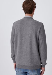 Felpa grigia con finitura a maglia testurizzata, scollatura a girocollo e polsini a costine. Abbinata a jeans blu casual.