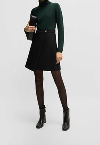 Svart kjol med en figurnära midja och silverdetalj i form av knappar, kombinerad med en mörkgrön polotröja och svarta anklarboots. Slät struktur overall.