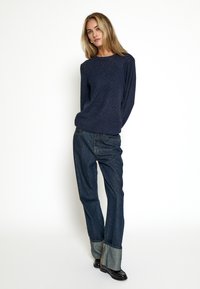 Mørkeblå strikket sweater med struktureret finish og diamantmønster, parret med løse, opsmøgede mørke denim jeans og blanke sorte støvler.