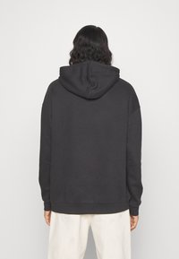 Sudadera con capucha negra de textura suave, ajuste holgado, hombros caídos y puños acanalados. El diseño incluye un bolsillo tipo canguro.