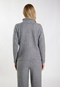 Pulover din tricot gri, cu un guler înalt, având mâneci lungi și o siluetă ajustată. Țesătura pare moale și texturată.