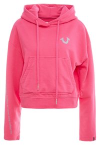 Sudadera corta rosa de algodón, con un bolsillo delantero, cordones y un logotipo plateado en el pecho. El texto se extiende por la manga izquierda.