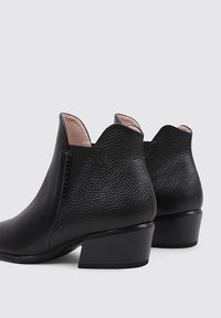 Botas de cuero negras a la altura del tobillo con un acabado texturizado, presenta un tacón bajo y detalles recortados en el tobillo.