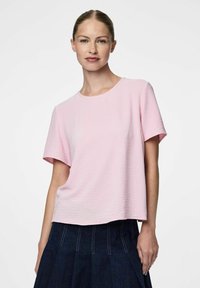 T-shirt rosa chiaro a maniche corte con finitura testurizzata, scollatura rotonda e vestibilità ampia. Abbinato a una gonna di denim scuro con cuciture bianche.