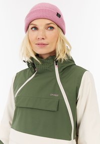 Groene en beige jas met een hoge kraag, ritssluiting en een voorktas. Voorzien van geperforeerde details en een roze beanie.