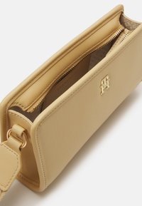 Beige skinnveske med glatt tekstur og gullfarget detaljer. Har en glidelåslomme og preget logo på forsiden.