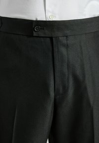 Pantalones formales negros hechos de un tejido texturizado, con un diseño de frente plano, dos bolsillos laterales y un cierre de botón único en la cintura.