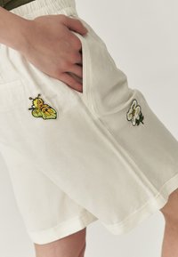 Shorts blancs en mélange de coton, dotés d'une poche latérale. Détails brodés d'un papillon et d'une fleur de chaque côté.