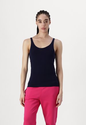 Débardeur bleu marine à fines bretelles et décolleté arrondi, fabriqué en tissu lisse. Associé à un pantalon de survêtement rose.