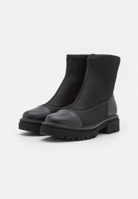 Par de botas negras hasta el tobillo con suelas gruesas y perfilado suave, fabricadas con materiales de tela y cuero.