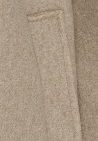 Beige uldstof med en tekstureret overflade og en lommedetalje. Materialet har en blød, let ru tekstur med subtile mønstre.